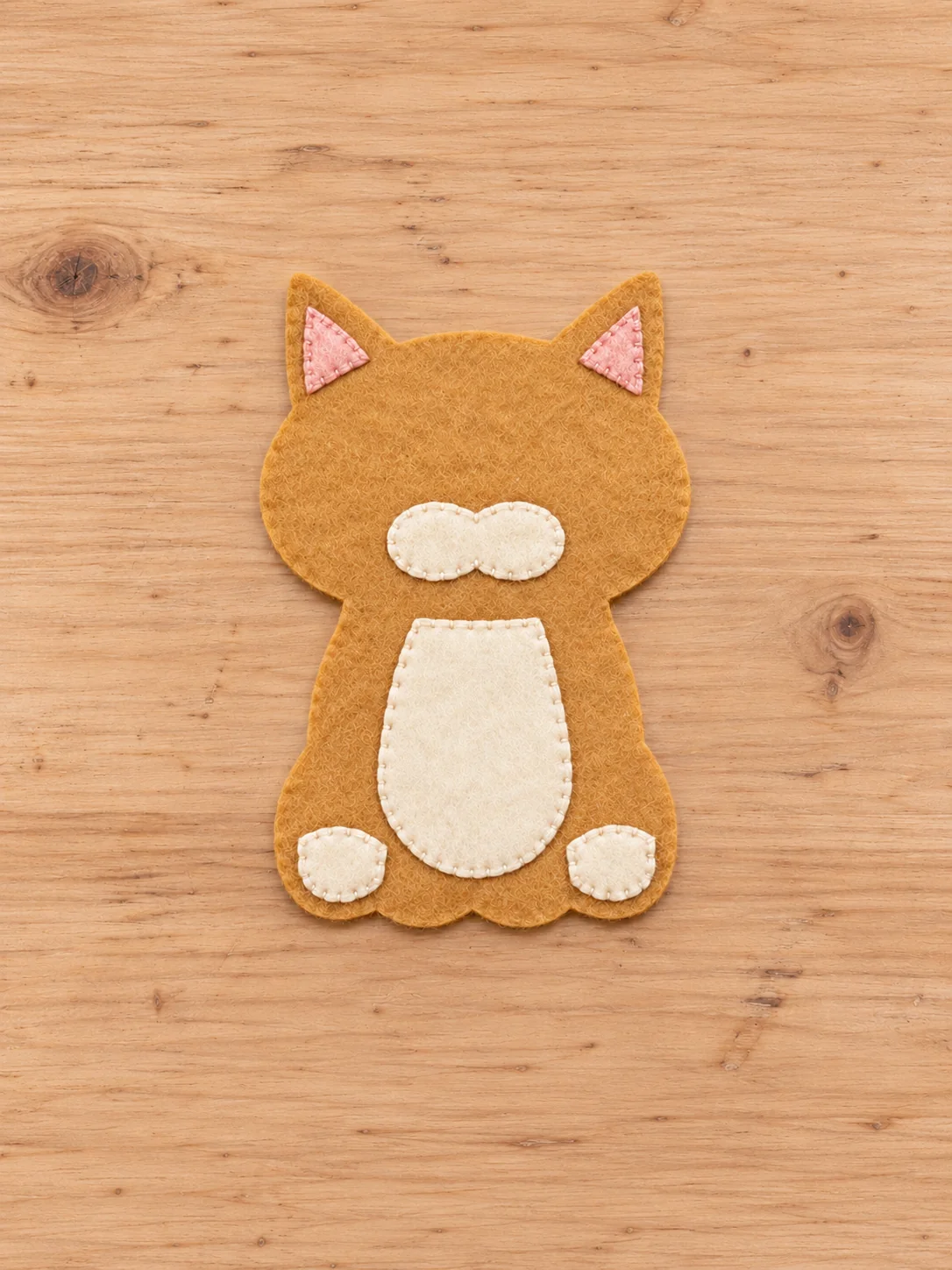 Pink inner ears and ivory muzzle belly and paws stitched to the tan felt cat front