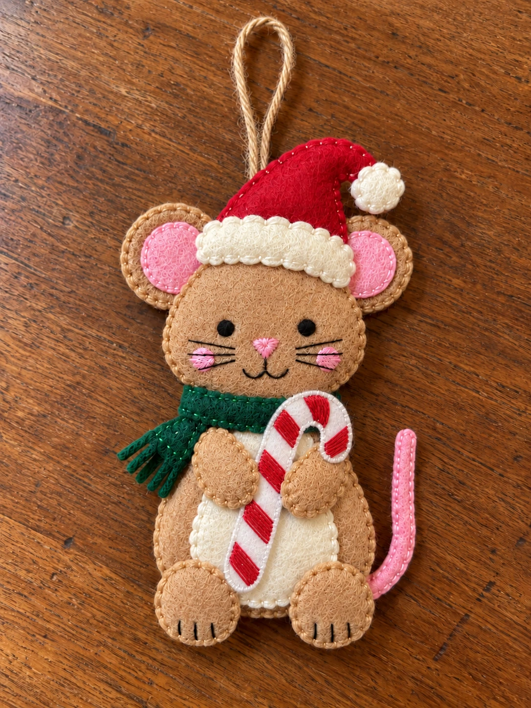 Hand-sewn felt Christmas mouse with a Santa hat, green scarf and striped candy cane resting on a wooden table