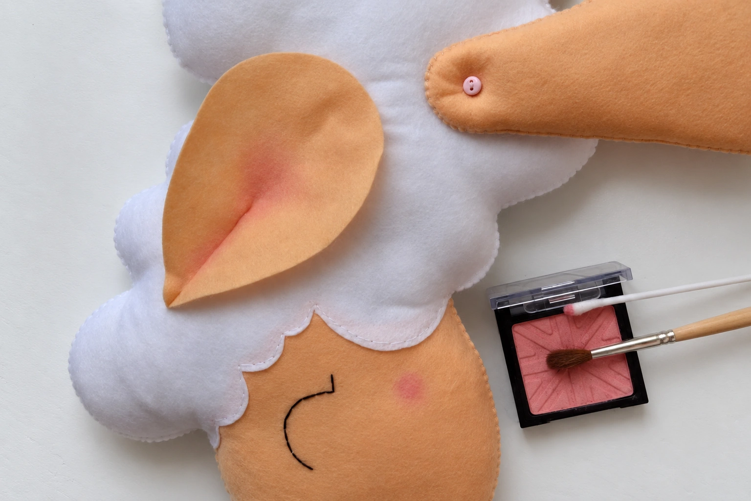 A small brush applying pink blush inside the folded beige ear