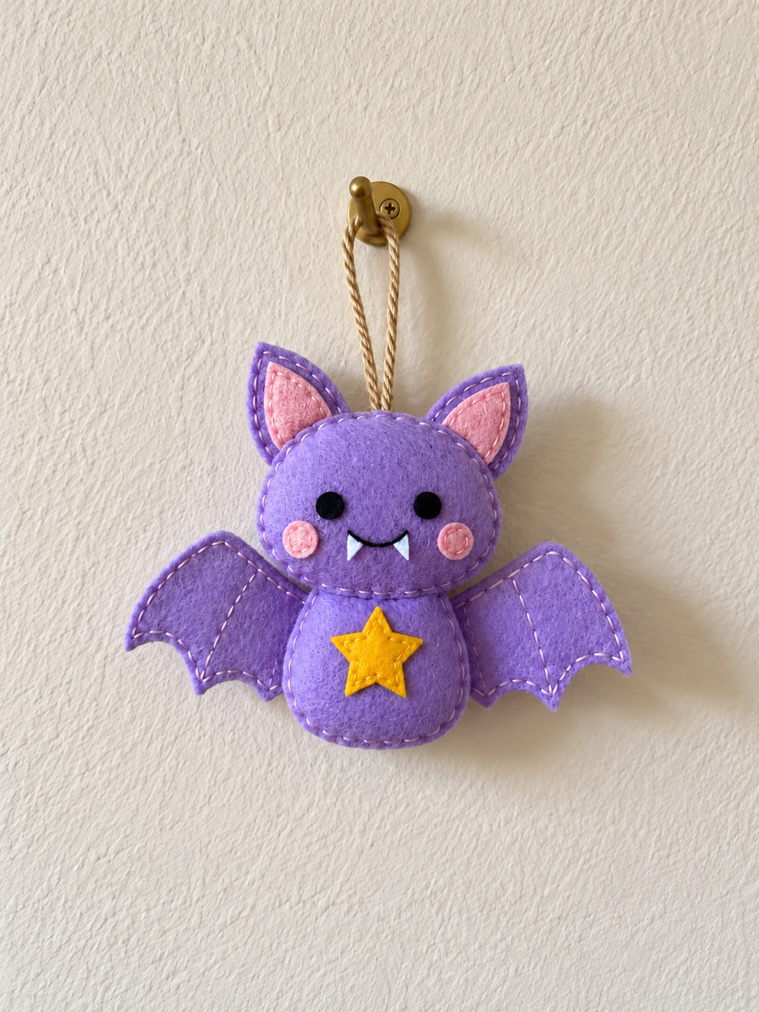 Matching lavender felt star bat ornament hanging from twine on a wall hook